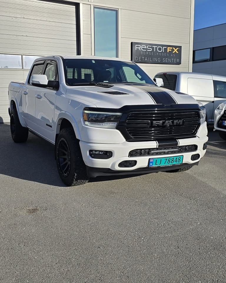 Hvit RAM 1500 med sorte striper foran skiltet på detaljsenteret